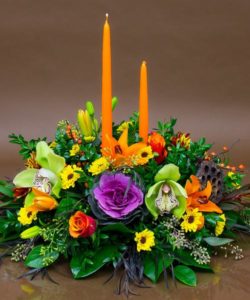 two orange candles in center of yellow and orange flowers and greenery