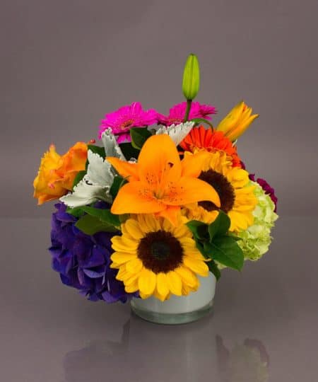 This bouquet is blooming with vibrant colors to bring a smile and delight to the face of that special recipient. Orange roses, pink Gerbera daisies, blue hydrangea and more are nestled together to create this eye catching design.